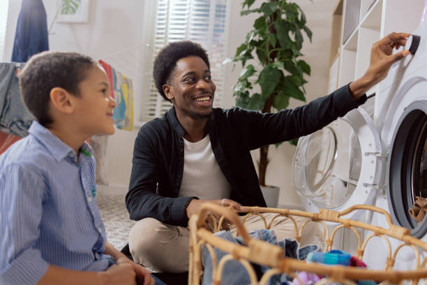 istock Dad spends time with young child in laundry room, bathroom, performs household duties while on paternity leave, takes care of son, shows boy how to operate washing machine 1422240453