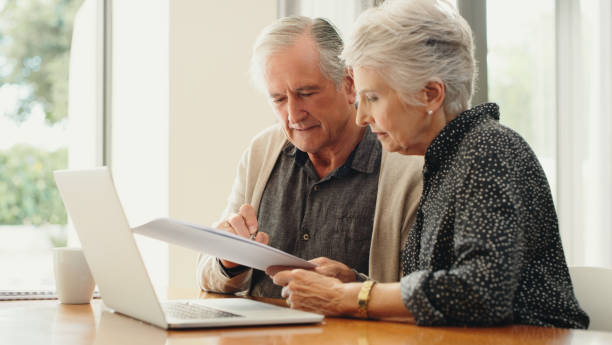 Senior couple with laptop and budget document, paperwork or finances for retirement plan, pension, funeral planning expenses. Married man and woman discuss their will and estate or mortgage home loan stock photo