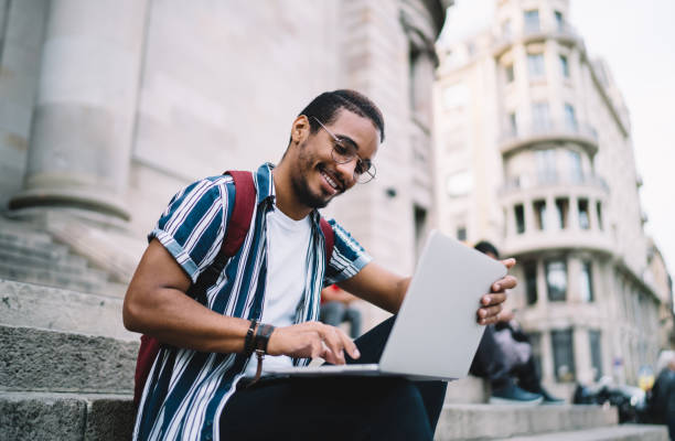 istock Cheerful dark skinned african american hipster guy typing on laptop computer share content via laptop computer and browsing, positive dark skinned male student satisfied with learning via webinars 1422242690