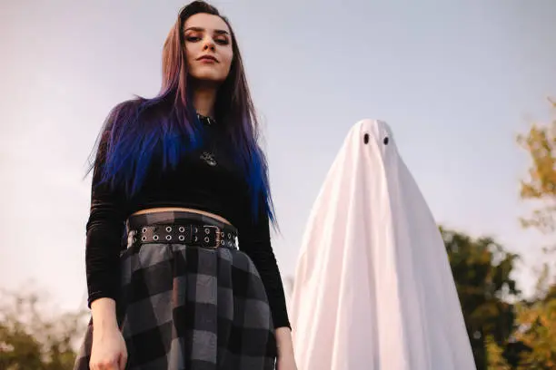 Happy young woman standing with ghost against blue sky outdoors during Halloween