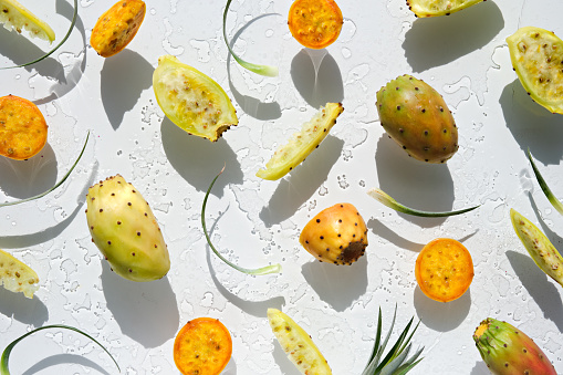 Exotic fruits, yellow and orange prickly pears, healthy cactus fruits on off white background with leaf. Flat lay, direct sunlight with shadows. Wet background with traces of water.