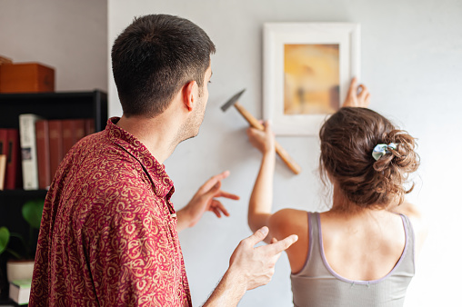 Young couple decorates their new apartment with painting on the wall