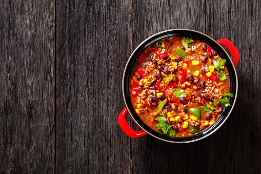 taco soup of ground beef, tomatoes, chopped green chilis, onions, corn, red beans and taco seasoning in red pot, high angle view, flat lay, close-up, free space