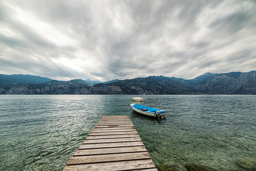 Wooden jetty facing western bank of Lake Garda, view from Malcesine beach. Lake Garda is the largest lake in Italy. It is a popular holiday location in northern Italy, about halfway between Brescia and Verona, and between Venice and Milan on the edge of the Dolomites.