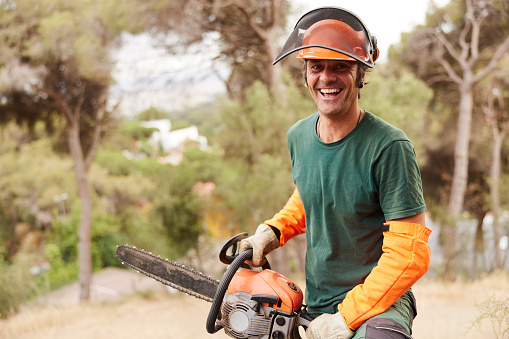 Waist-up portrait of a smiling man who holds a chainsaw.
