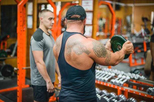 istock Man doing exercises in the gym with a man trainer athletic physique 1422258709