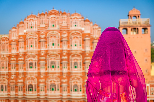 Young Indian woman, wearing sari, posing next to Hawa Mahal Palace, Jaipur, Rajasthan. The Hawa Mahal is the palace in the city of Jaipur - built from red and pink sandstone, it is on the edge of the City Palace.