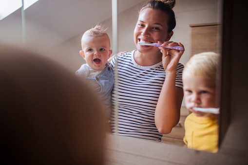 Young mother and two sons look at each other in the mirror while brushing their teeth