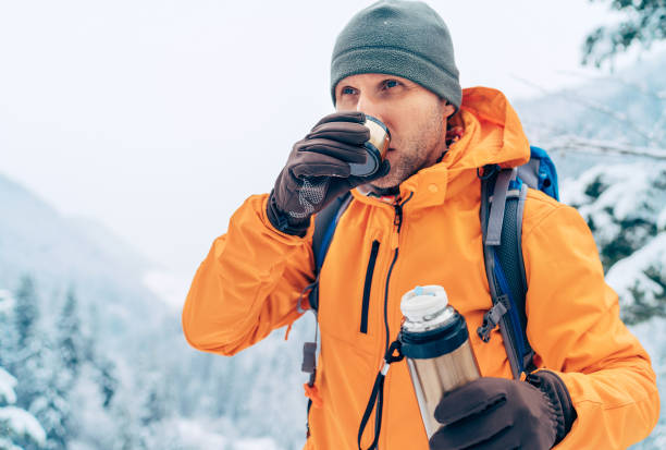Man drinking a hot drink from thermos flask dressed bright orange softshell jacket while he trekking winter mountains route. Active people in the nature concept image. stock photo