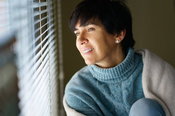istock Happy middle-aged woman smiling while looking out the window. 1422272731