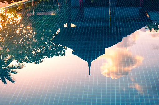 Reflection in the pool on the surface of the water entrance to the villa and a tree with frangipani flowers. Rest and relaxation.