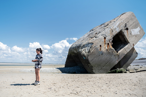 side view on girl standing in front of old huge german concrete bunker at french beach on sunny summer day