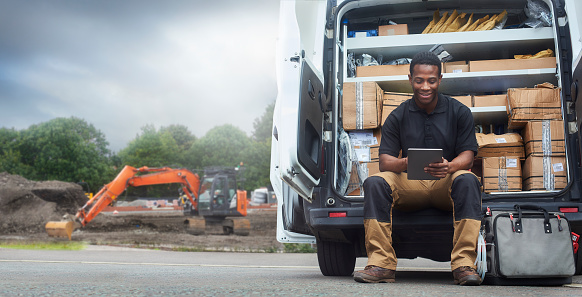 A Service engineer sat on the back step of his van using a digital tablet