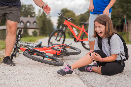 People approach a young girl shouting and screaming in pain after falling from a bicycle