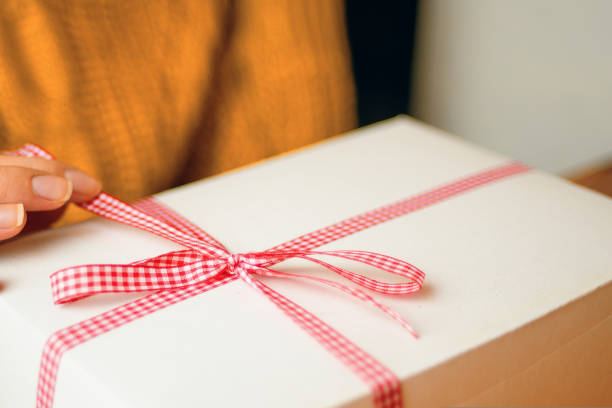 istock Women's fingers hold red checkered ribbon on gift box. 1422293412