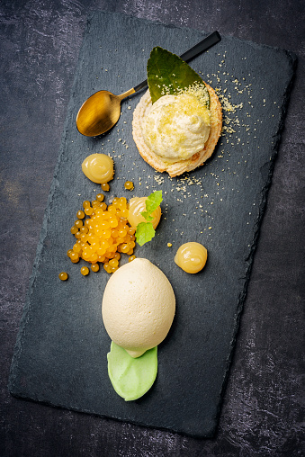 Lemon themed dessert close-up. The dessert consists of a lemon flavoured and lemon shaped cake, a limoncello kransekake with lemon pearls and lemon curd. Colour, vertical format with some copy space. Photographed on location in restaurant on the island of Moen in Denmark.