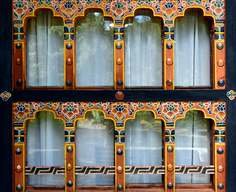 Paro, Bhutan: double tiered trefoil timber windows ('payab gochu', of the 'horgo payab' type) with horzhu floral decoration and kachung ornamentation of the mullion. By a 1998 royal decree, all buildings must be constructed with multi-coloured wood frontages, small arched windows, and sloping roofs. Modern facades, look very similar to old buildings. Bhutanese Architecture.