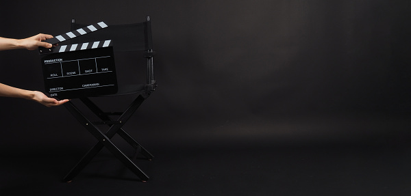 Black Director chair and hand is hold clapper board or movie slate on black blackground.