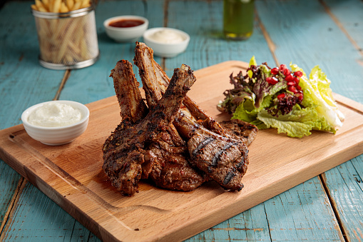 spicy Lamb chops with salad, mayo dip, chili sauce and fries isolated on cutting board side view fastfood