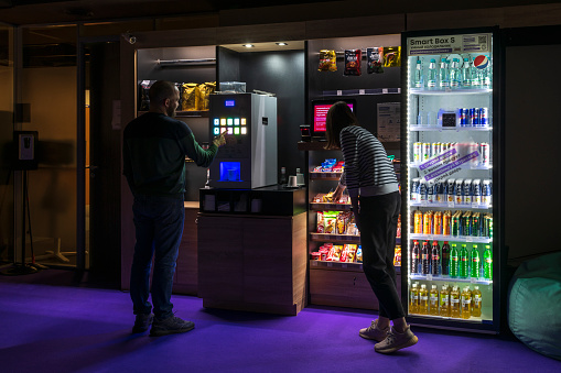 Russia, Moscow - February 11, 2022: People buys coffee and food in micro market (unmanned self service smart store) in night office. Food service theme.
