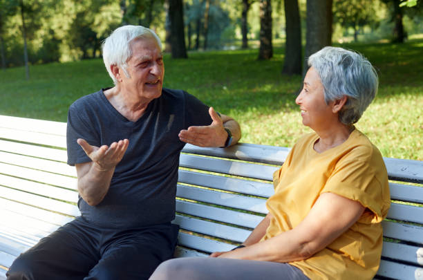 istock Older couple talking seated on bench in summer park 1422312346