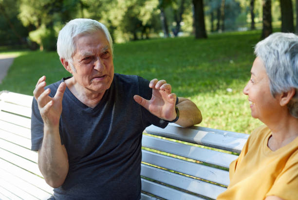 istock Older couple talking seated on bench in summer park 1422312347