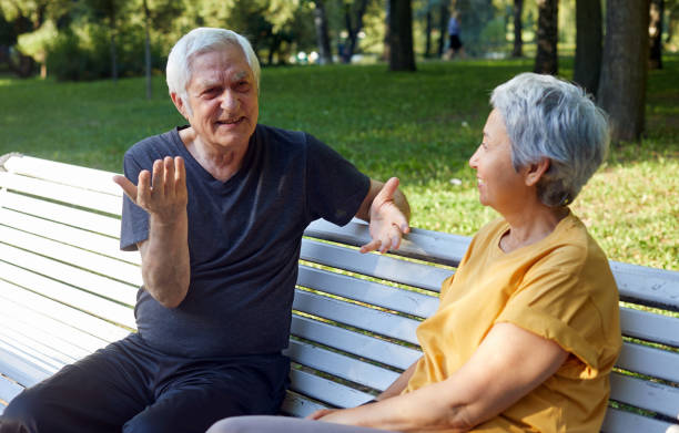 istock Older couple talking seated on bench in summer park 1422312348