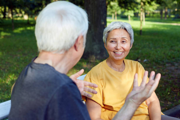 istock Older couple talking seated on bench in summer park 1422312351