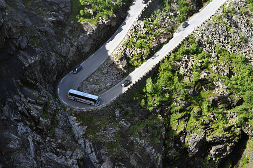 A large bus full of tourists tries to dial in a narrow bend on a winding troll road in Norway-