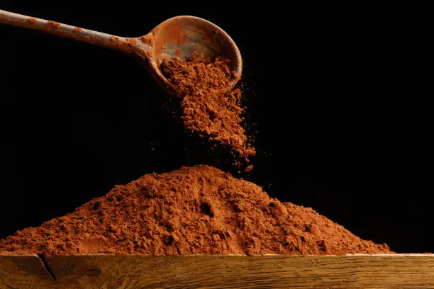 Falling chocolate powder on wooden table from a spoon. Shallow depth of field.