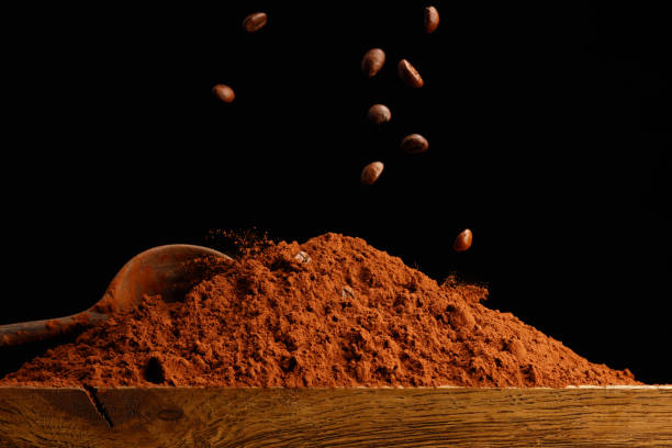 Falling coffee beans in a heap of cocoa or chocolate powder .