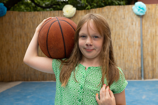 Beautiful toddler playing with basketball ball around lots of toys smiling at kindergarten