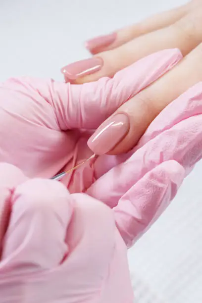 Close up process of applying clear nail polish. Woman in salon receiving manicure by nail beautician. Pink nail varnish and brush, macro. Shallow depth of field