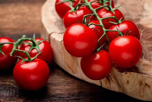 Branch of fresh cherry tomatoes on a brown wooden background.