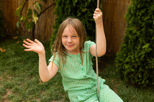 Portrait of active young 7 year's old Caucasian girl swinging on a rope swing and waving