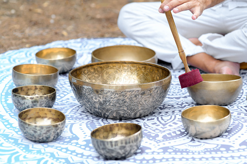 Close-up of man hands playing on a singing tibetian bowl with sticks. Sound healing music instruments for meditation, relaxation, yoga. Sound therapy. Buddhist healing practices.Selective focus