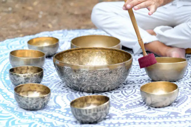 Close-up of man hands playing on a singing tibetian bowl with sticks. Sound healing music instruments for meditation, relaxation, yoga. Sound therapy. Buddhist healing practices.Selective focus