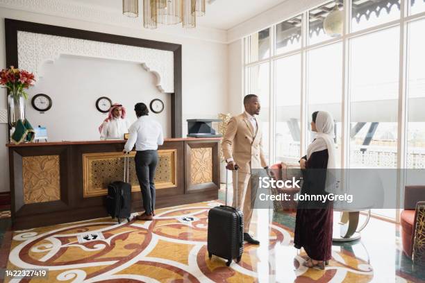 Hotel Guests Standing In Lobby And At Reception Desk Stock Photo - Download Image Now