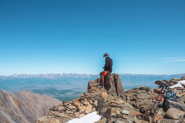 Tourist sitting on stone near abyss edge on high altitude under blue sky in sunny day. Man with camera on high rock near precipice edge with wonderful view from above to large mountain range in away. turista sentado en piedra cerca del borde del abismo a gran altitud bajo el cielo azul en un día soleado. hombre con cámara en la roca alta cerca del borde del precipicio con una vista maravillosa desde arriba a una gran cordillera en la distancia.