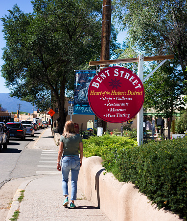 Taos, NM: A tourist walks past a “Bent Street” sign on a sunny sidewalk in downtown Taos.