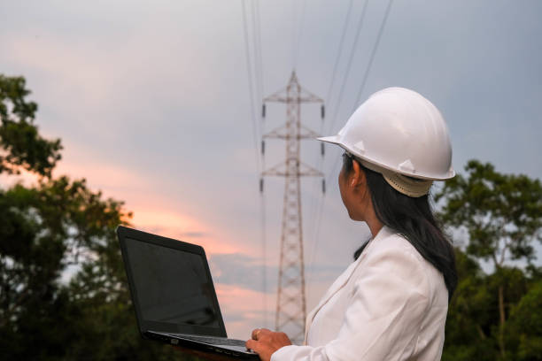 istock Asian female electrical engineer working on laptop near high voltage pole, inspecting power grid. Wind Turbine Engineer for Electric Power Generation. renewable energy concept 1422379477