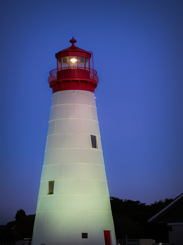 Red and metallic lighthouse with light beam at sunset with clouds