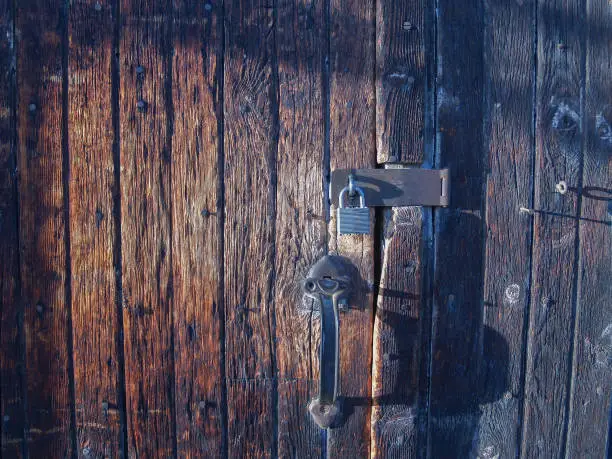 Old wooden door made of vertical planks worn and faded with padlock and handle.