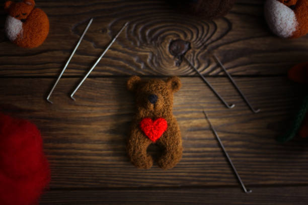 toy bear cub with heart made of wool and tools for dry felting, dark brown wooden background