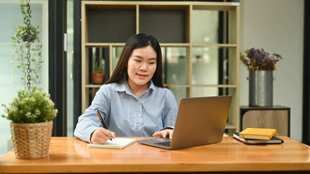 istock Beautiful female employee using laptop computer at bright modern corporate office. 1422406077