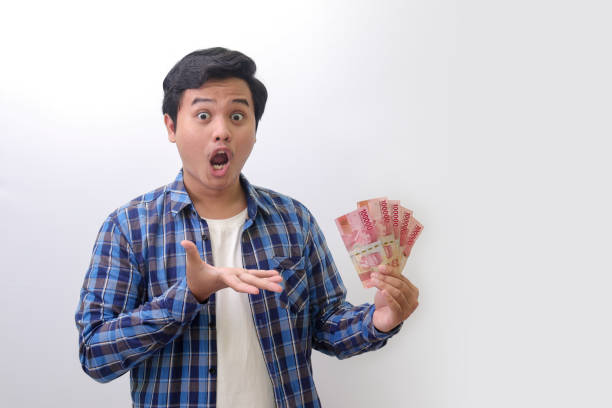 istock excited Asian man standing against white background, showing one hundred thousand rupiah while making surprise hand gesture 1422406713