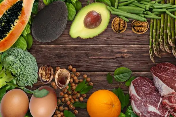 Photo of Natural sources of folic acid . Foods as papaya Avocado, eggs, orange, broccoli, liver, asparagus, beans, spinach, nuts and seeds  on wooden table.