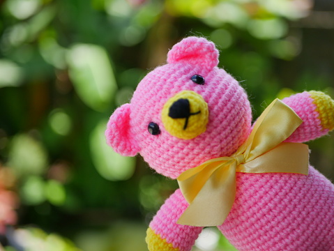 pink crocheted bear (amigurumi) yellow bow tie knitted with yarn on a green background