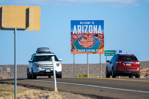 A welcome to Arizona sign seen next to the highway in the desert landscape. Two cars passing by going different directions. Seen at day in Arizona, USA.