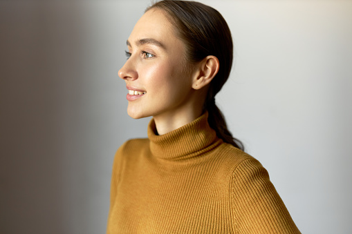Close-up profile view image of lovely charming curious creative pensive smiling inspired millennial girl dressed in turtleneck, looking aside with enthusiasm, isolated on white background